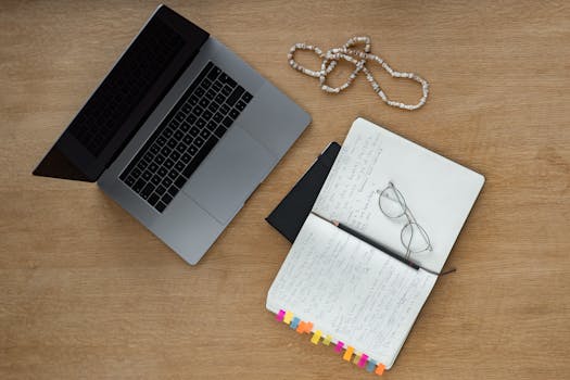 A neat desk setup with laptop, notebook, and glasses on a wooden surface, perfect for studying or working from home.